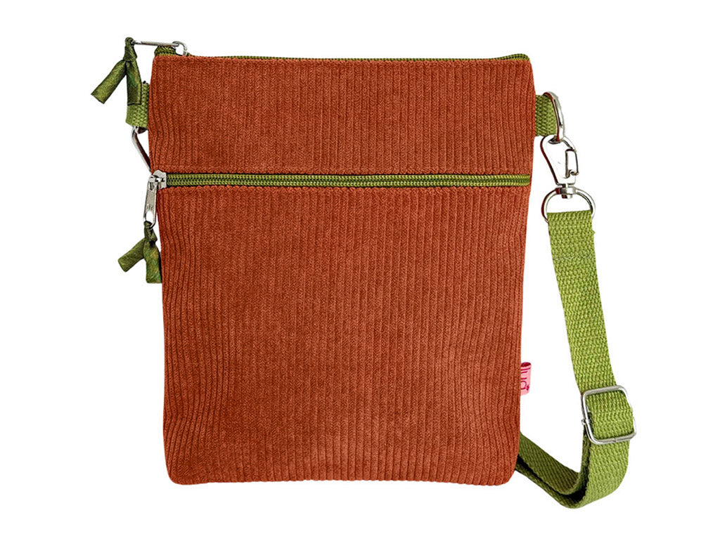 A small rectangular crossbody bag made of rust-orange corduroy fabric with an olive green zipper and a matching green adjustable shoulder strap, shown on a plain white background.