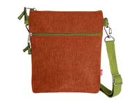 A small rectangular crossbody bag made of rust-orange corduroy fabric with an olive green zipper and a matching green adjustable shoulder strap, shown on a plain white background.