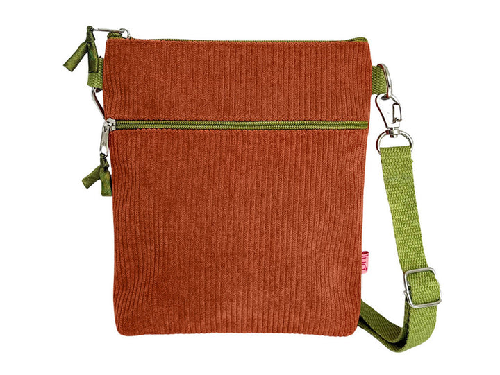 A small rectangular crossbody bag made of rust-orange corduroy fabric with an olive green zipper and a matching green adjustable shoulder strap, shown on a plain white background.