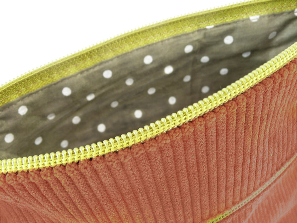 Close-up of an open zippered pouch showing a ribbed dusty rose exterior, a yellow zipper, and a gray interior with white polka dots.