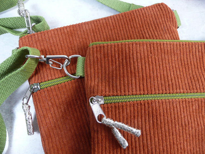 Two brown corduroy zippered pouches with green zipper trim and green webbing straps, shown on a light background.