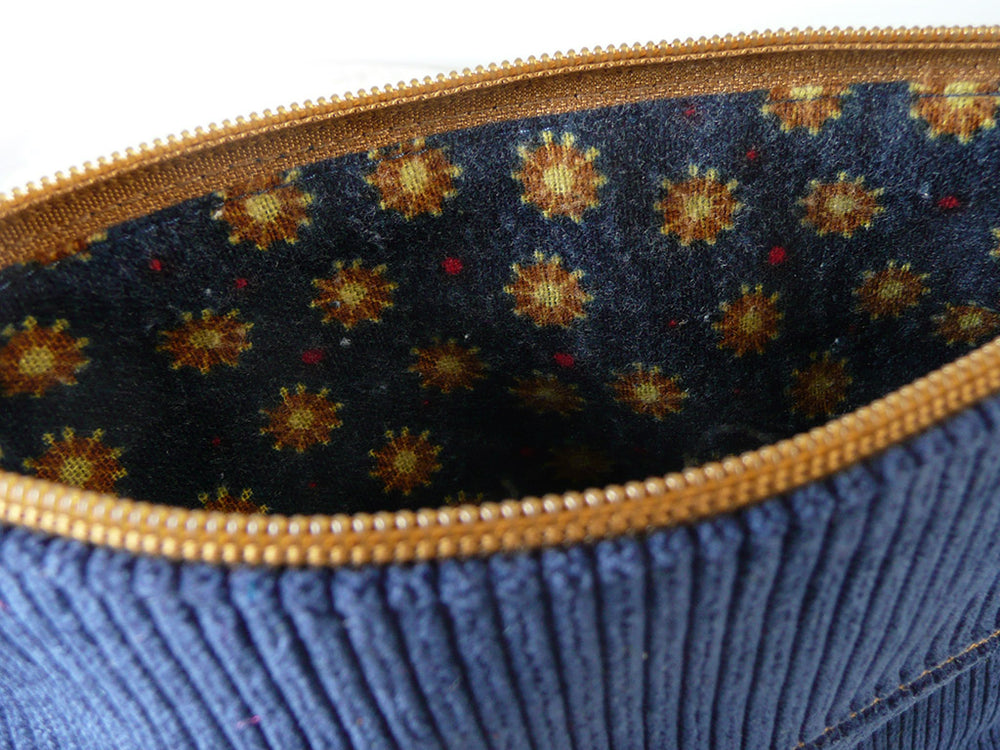 Close-up of the inside of a blue corduroy zipper pouch or bag, showing a navy patterned lining with gold and red starburst motifs and a gold zipper.