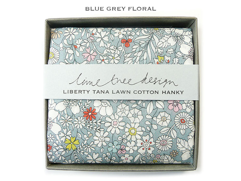 A folded floral cotton hanky in a gray gift box with a white paper band reading &