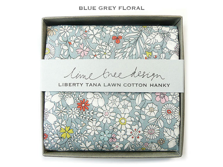 A folded floral cotton hanky in a gray gift box with a white paper band reading &