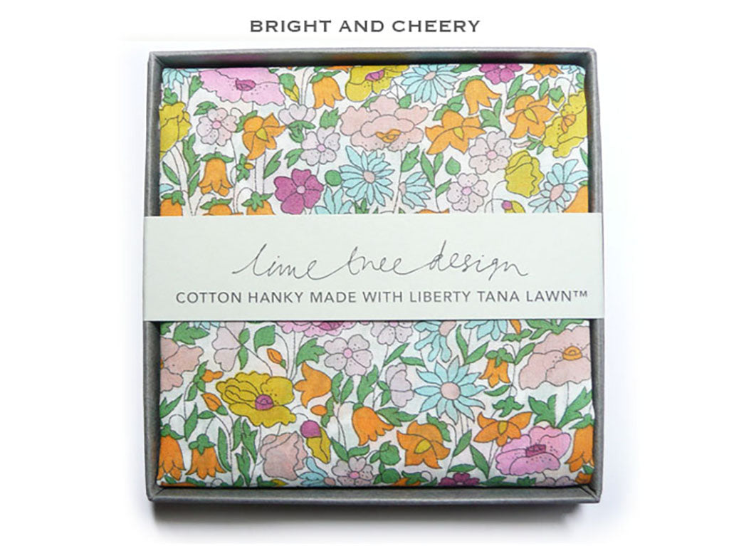 A folded cotton hanky with a colorful floral print in yellow, pink, orange, and blue, presented in a gray gift box with a white paper band reading &