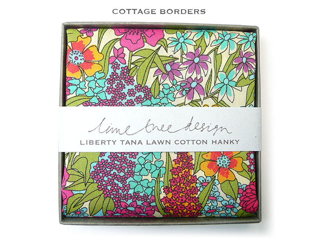 A folded cotton hanky with a colorful floral print in yellow, pink, orange, and blue, presented in a gray gift box with a white paper band reading &