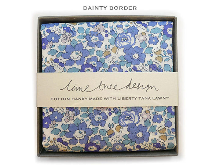 A folded cotton hanky with a blue, purple, and beige floral pattern, presented in a dark gray box with a beige paper band reading &
