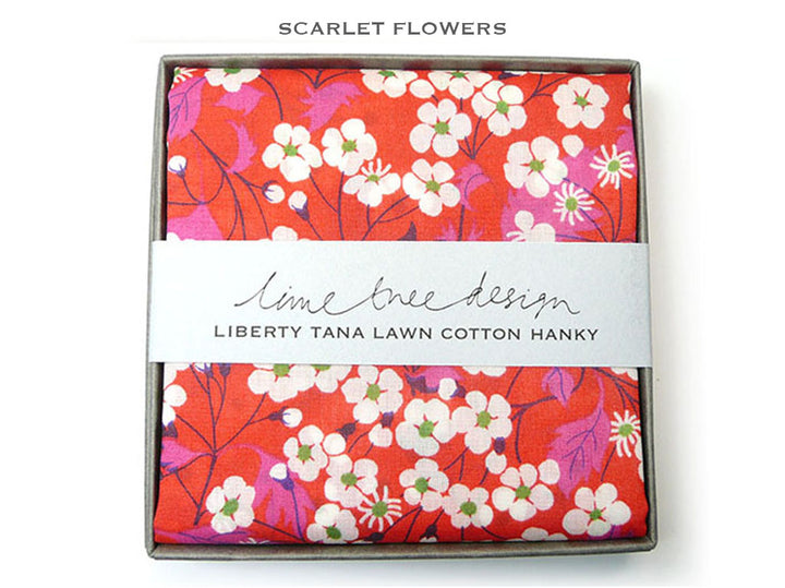 A folded cotton hanky with a bright red, pink, and white floral print, presented in a square gray box with a white paper band reading &
