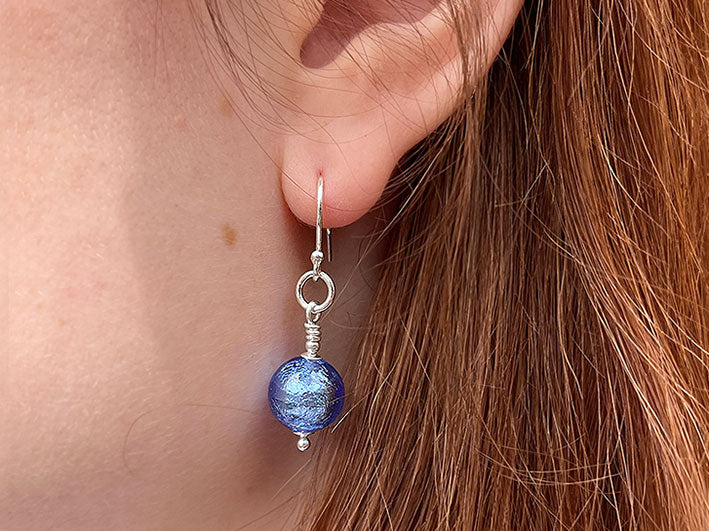 Model shown wearing a simple blue glass and silver earring with warm chestnut hair.