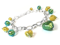 A silver chain charm bracelet featuring green and yellow heart-shaped glass beads and smaller metallic beads, displayed on a clean white background.