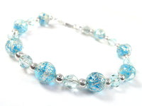 A beaded bracelet featuring light blue glass beads with metallic silver crackle patterns, alternating with faceted clear glass beads and polished silver spacer beads, set against a plain white background.