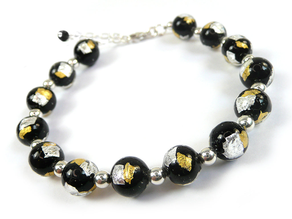 A beaded bracelet featuring glossy black glass beads with embedded metallic gold and silver leaf, separated by small polished silver spacer beads, on a white background.