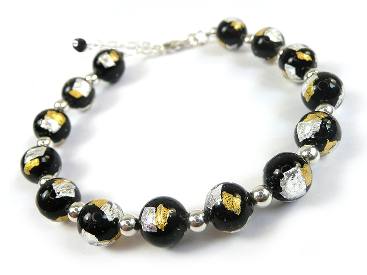 A beaded bracelet featuring glossy black glass beads with embedded metallic gold and silver leaf, separated by small polished silver spacer beads, on a white background.