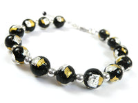 A beaded stretch bracelet featuring glossy black glass beads with embedded gold and silver leaf, separated by small polished silver spacer beads, on a white background.