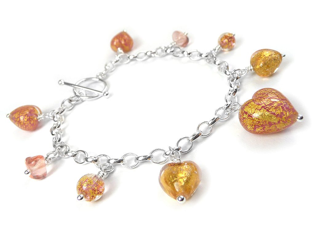 A silver chain bracelet with a toggle clasp and multiple dangling heart-shaped glass charms in orange, peach, and gold glitter, displayed on a clean white background.