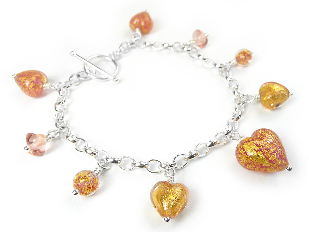 A silver chain bracelet with multiple dangling heart-shaped and teardrop-shaped glass charms in shimmering gold, orange, and pink tones, shown on a plain white background.