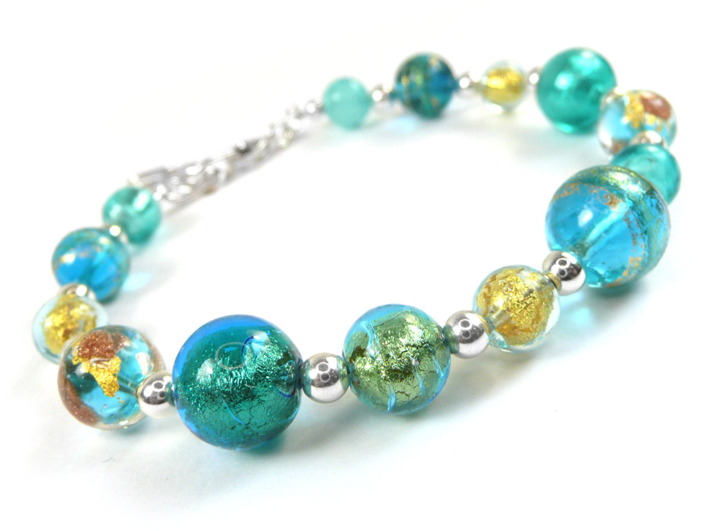 A beaded bracelet featuring translucent turquoise, teal, and blue glass beads, some with gold leaf inclusions, separated by small silver spacer beads, and finished with a silver clasp, shown on a white background.
