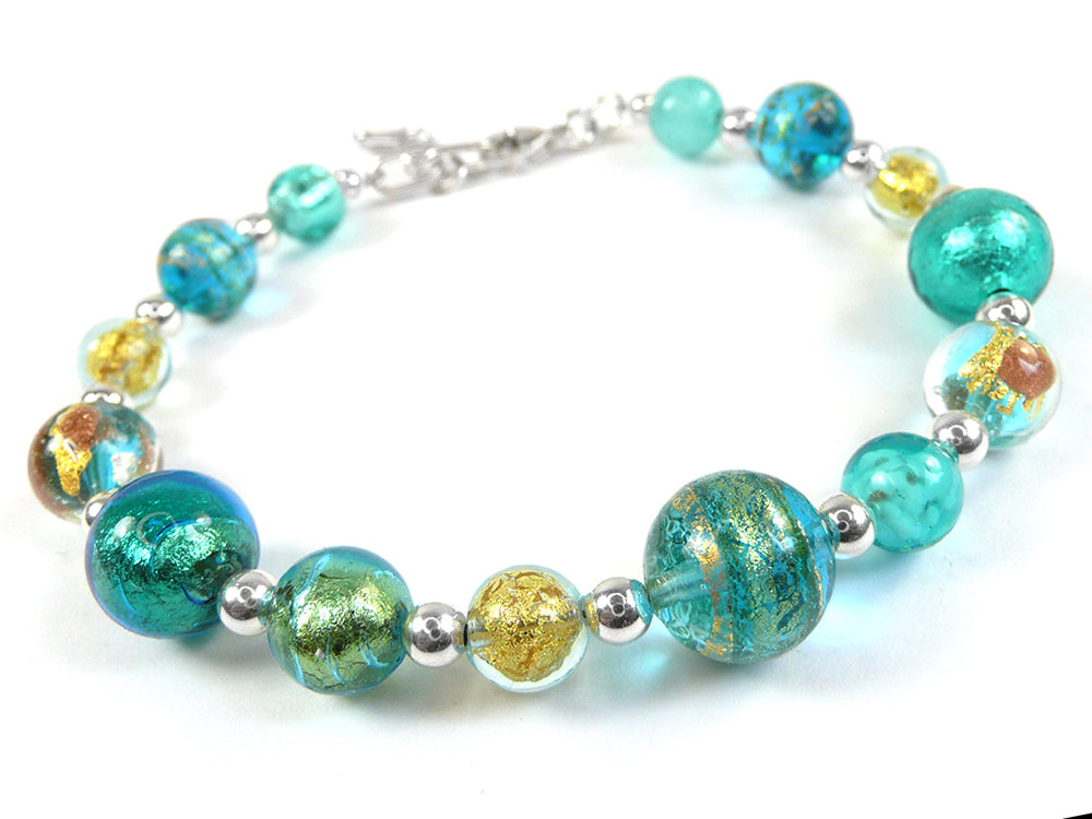 A beaded bracelet featuring textured turquoise, teal, and green glass beads with gold leaf accents, separated by small silver spacer beads, on a white background.