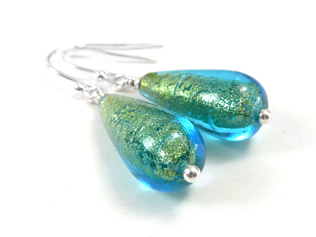 A pair of teardrop-shaped glass dangle earrings with shimmering green and blue glass beads, suspended from silver fishhook wires on a white background.