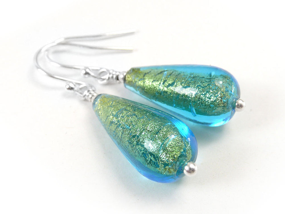 A pair of teardrop-shaped glass dangle earrings with a blue and green iridescent finish, featuring silver-toned metal hooks and beads on a plain white background.