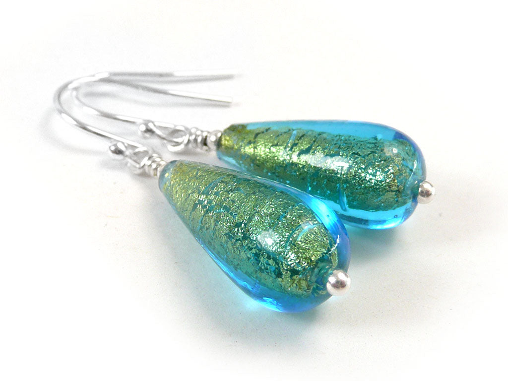 A pair of handmade teardrop-shaped glass drop earrings with a vibrant blue and green glitter finish, attached to silver fishhook ear wires on a clean white background.