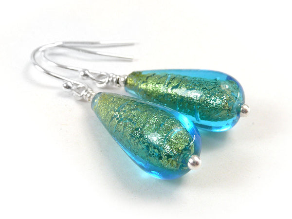 A pair of handmade teardrop-shaped glass drop earrings with a vibrant blue and green glitter finish, attached to silver fishhook ear wires on a clean white background.
