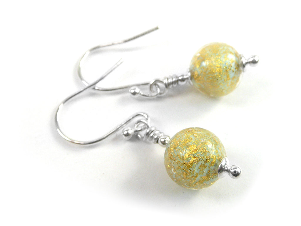 A pair of handmade dangle earrings featuring round, textured gold and light blue beads with fine glitter, suspended from silver-tone French hook wires on a white background.
