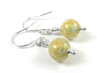 A pair of handmade dangle earrings featuring round, textured gold and light blue beads with fine glitter, suspended from silver-tone French hook wires on a white background.