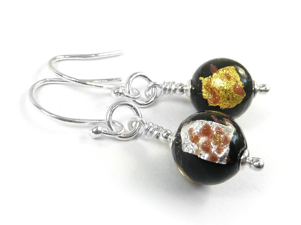 A pair of earrings featuring round glass beads in black with silver and gold foils on silver earwires on a white background.