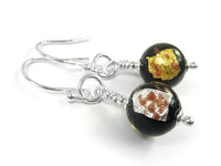 A pair of earrings featuring round glass beads in black with silver and gold foils on silver earwires on a white background.