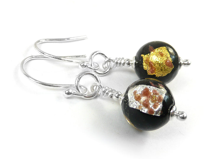A pair of earrings featuring round glass beads in black with silver and gold foils on silver earwires on a white background.