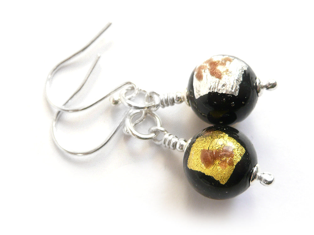 A pair of earrings featuring round glass beads in black with silver and gold foils on silver earwires on a white background.