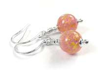 A pair of handmade dangle earrings featuring round pink glass beads with gold glitter flecks, suspended from silver-toned French hook wires on a white background.