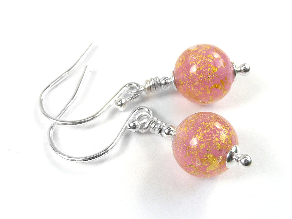 A pair of handmade dangle earrings featuring round pink glass beads filled with gold glitter, suspended from silver-colored wire-wrapped hooks on a white background.