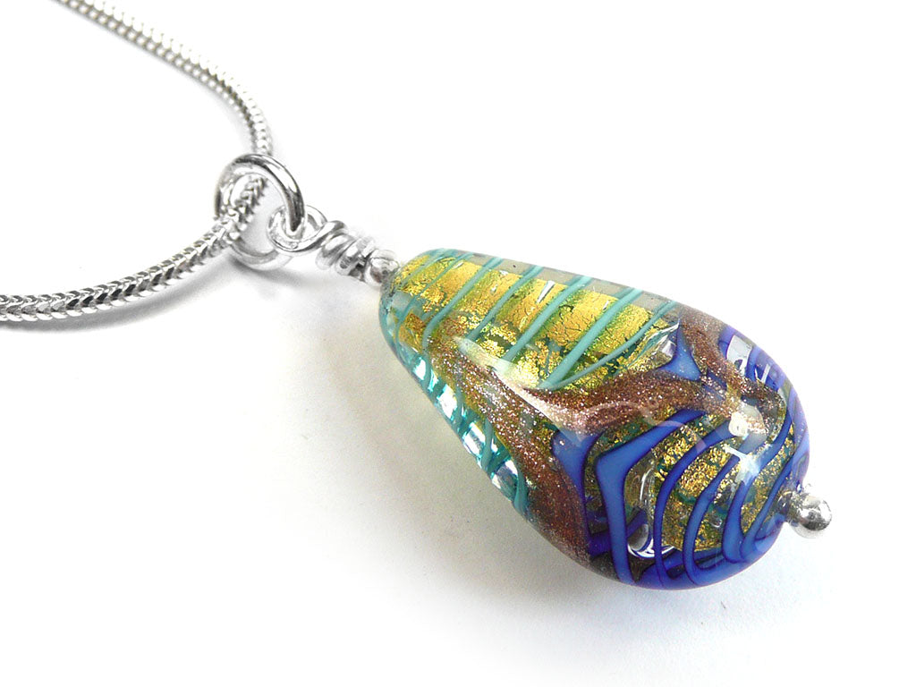 A close-up of a teardrop-shaped glass pendant necklace on a silver chain, featuring swirls of blue, green, gold, and brown on a white background.