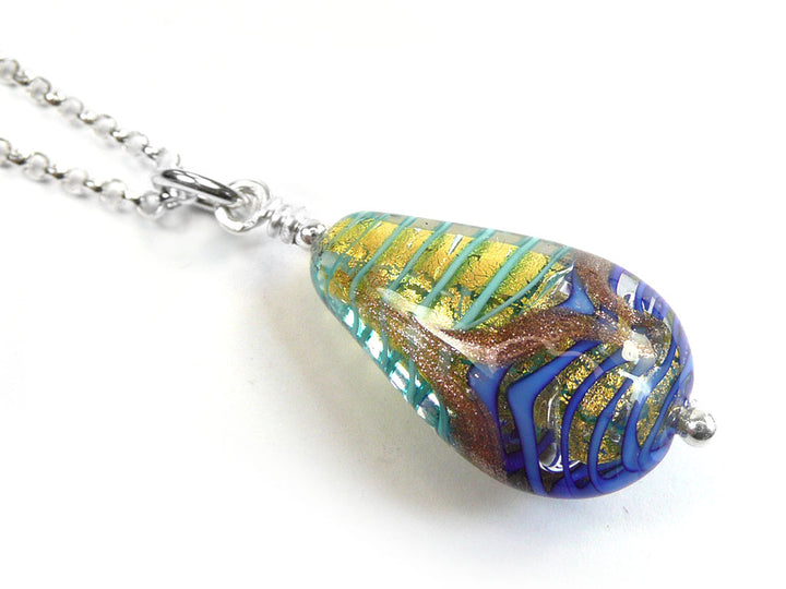 A teardrop-shaped glass pendant necklace on a silver chain, featuring a swirl pattern of blue, green, gold, and brown on a white background.