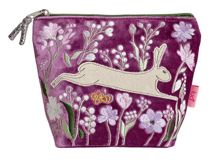 A magenta velvet zippered pouch featuring an embroidered design of a white hare, pink and white flowers, green leaves, and a small yellow bee. A pink tag on the right side reads &