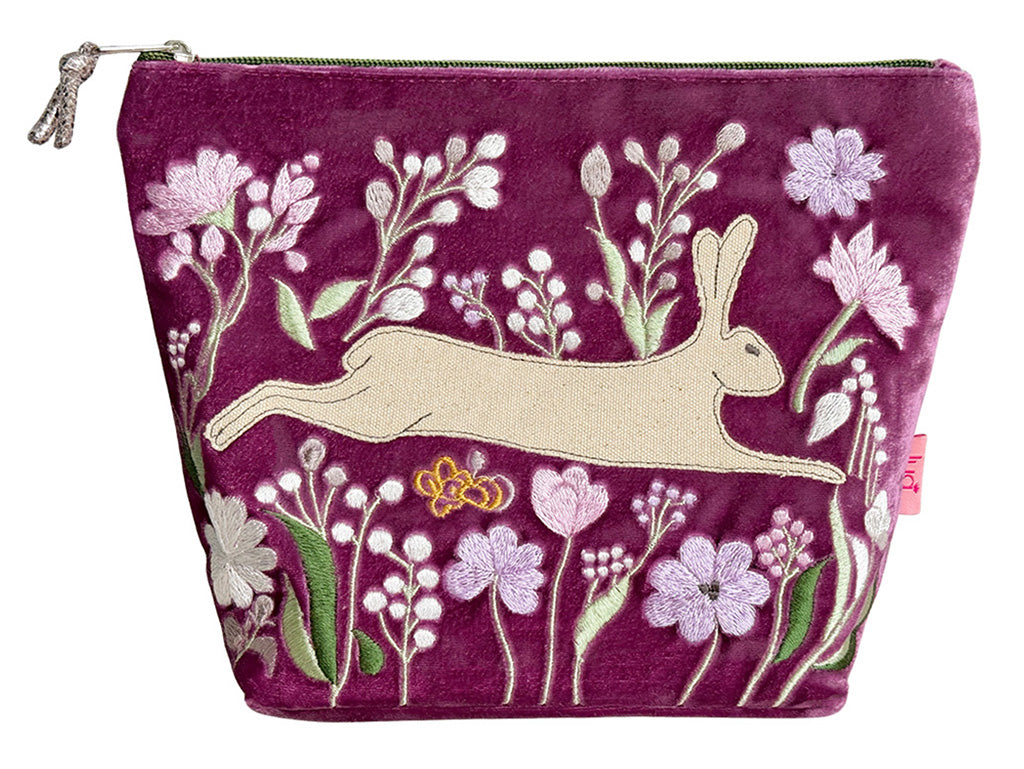 A magenta velvet zippered pouch featuring an embroidered design of a beige hare surrounded by pink, white, and green flowers.