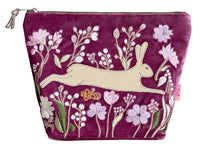 A magenta velvet zippered pouch featuring an embroidered design of a beige hare surrounded by pink, white, and green flowers.