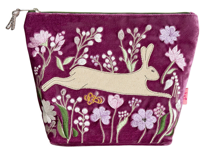 A magenta velvet zippered pouch featuring an embroidered design of a beige hare surrounded by pink, white, and green flowers.