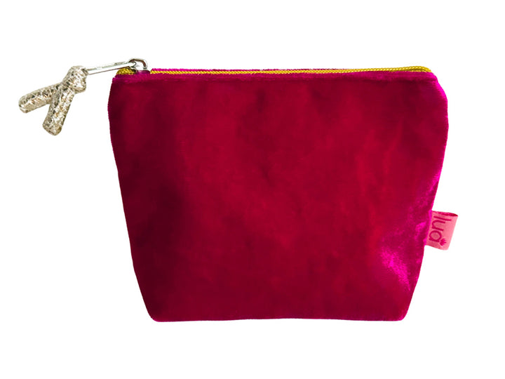 A small velvet pouch in a vibrant cerise pink colour, featuring a zipper and a silver glittery pull on the zip. A small pink fabric tag with the brand name &