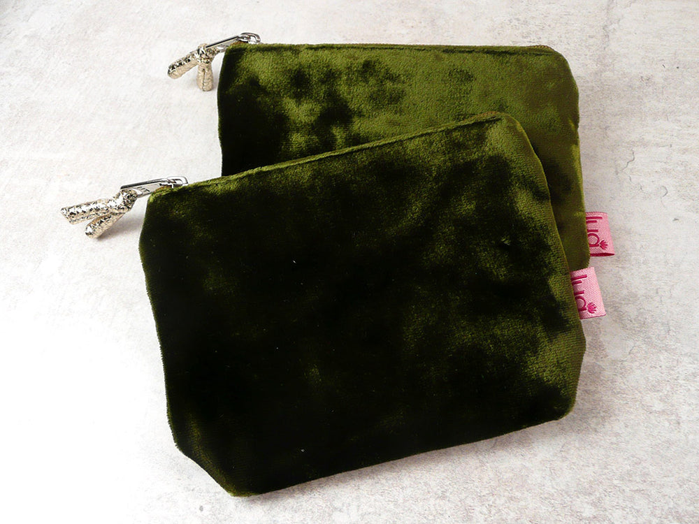 Two olive green velvet zippered pouches with silver-tone hardware and pink brand tags, displayed on a light textured background.