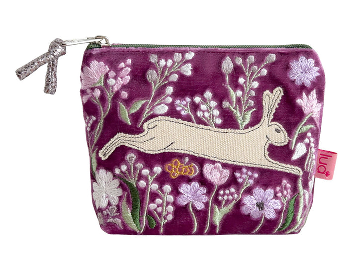 A small zippered pouch in magenta velvet with embroidered white and pink wildflowers, a cream hare, and a small gold bee. A pink tag on the right side reads &