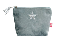 A small pale blue velvet pouch with a silver glittery star on the front, a silver zipper with a tassel pull, and a pink fabric tag on the side.