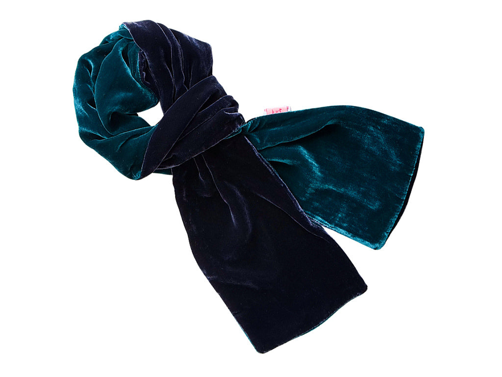A velvet scarf in a two-tone design of deep teal green and dark navy blue, styled in a loose knot on a plain white background.