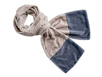 A plush velvet scarf with a colour-blocked design, featuring a light taupe-beige side and a dark slate-blue side, styled in a loose knot on a plain white background.