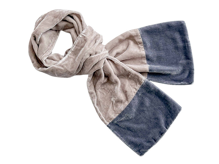 A plush velvet scarf with a colour-blocked design, featuring a light taupe-beige side and a dark slate-blue side, styled in a loose knot on a plain white background.