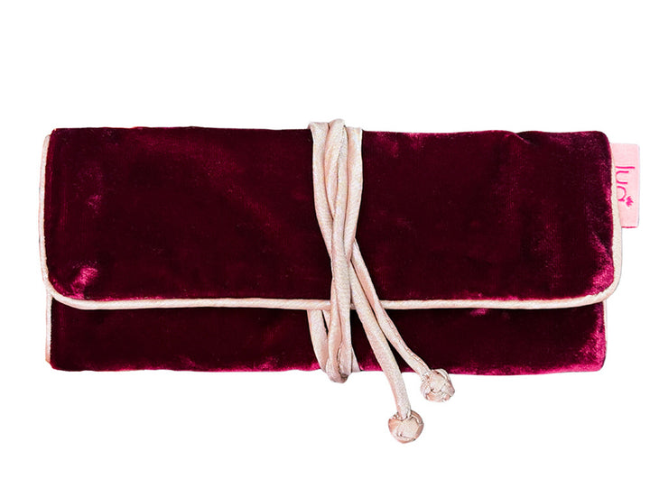 A burgundy velvet jewellery roll with a pale pink drawstring closure and a small pink brand tag on the side, shown against a plain white background.