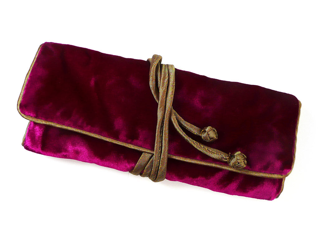 A deep magenta velvet clutch or pouch with gold trim and a brown rope tie, shown on a plain white background.