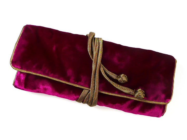 A deep magenta velvet clutch or pouch with gold trim and a brown rope tie, shown on a plain white background.